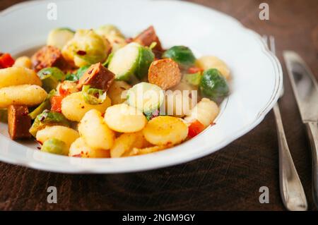 Plate with gnocchi, served with Brussel sprouts and vegan hot dog pieces. Stock Photo