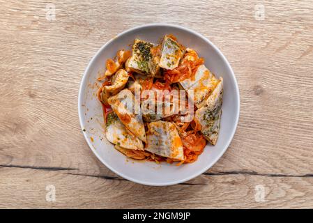 Raw herring in oil with paprika and cucumber, standing in a white plate on table. Stock Photo