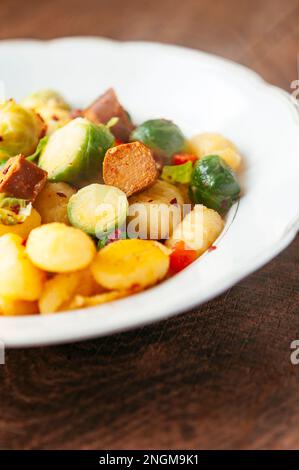 Plate with gnocchi, served with Brussel sprouts and vegan hot dog pieces. Stock Photo