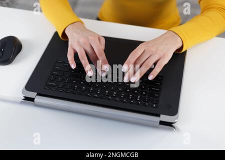Young woman typing text on laptop keyboard. Overhead photo of female person working on modern notebook computer behind white desk. Focus on beautiful Stock Photo