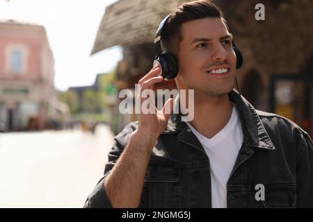 Handsome man with headphones listening to music on city street, space for text Stock Photo