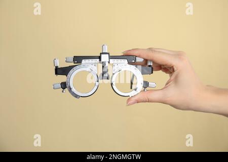 Woman holding trial frame on beige background, closeup. Ophthalmologist tool Stock Photo