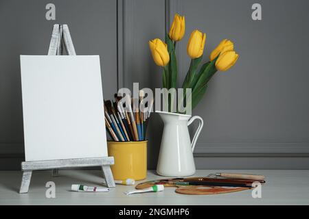 Easel with blank canvas, brushes, paints and palette in studio Stock Photo