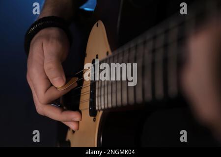 Man playing electric guitar on dark background, closeup. Rock music Stock Photo