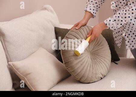 Young woman cleaning pillow with lint roller on sofa, closeup Stock Photo
