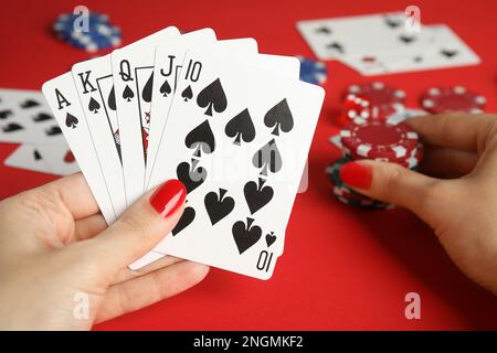 Woman holding playing cards with royal flush combination and poker chips at red table, closeup Stock Photo