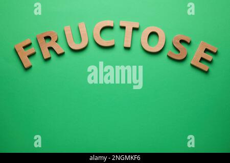 Word Fructose made of wooden letters on green background, flat lay. Space for text Stock Photo