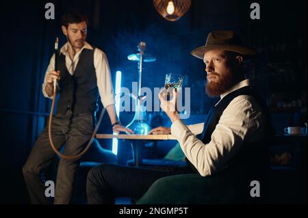 Serious guys smoking hookah while rest in pub Stock Photo