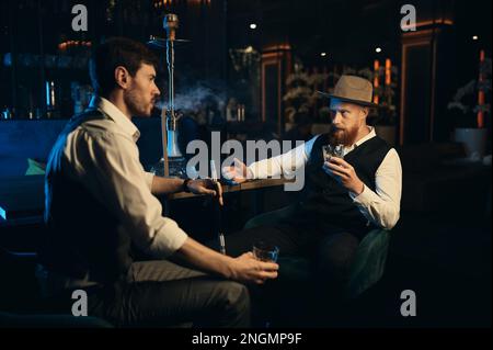 Guys having serious conversation while sitting face to face at hookah bar Stock Photo