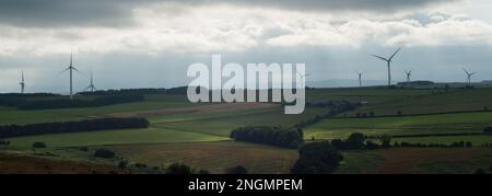 Landscape showing bright patches of sunlight breaking through clouds with wind turbines in the distance Stock Photo