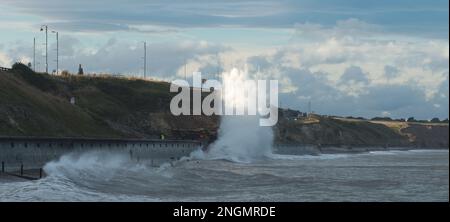 Powerful waves smash onto the promenade at Seaham throwing up a huge plume of spray caught by the late afternoon sun Stock Photo