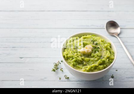 Delicate mashed potatoes with green peas, flavored with butter, spices and thyme on a light blue background. delicious homemade food. copy space Stock Photo