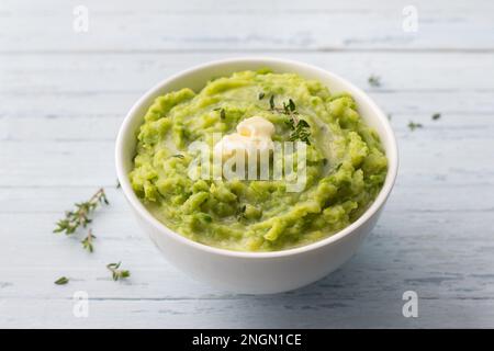 Delicate mashed potatoes with green peas, flavored with butter, spices and thyme on a light blue background. delicious homemade food Stock Photo