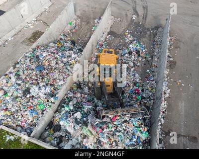 Skid steer loader moving plastic garbage with scrap grapple on the landfill site, drone shot. Waste disposal concept. Stock Photo