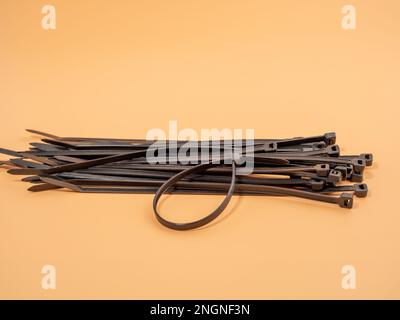 Black plastic cable ties on an orange background. Close-up. Stock Photo