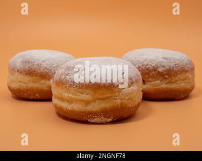 Freshly baked and dusted with powdered sugar German donuts. Donut berliner or krapfen on orange background. Stock Photo