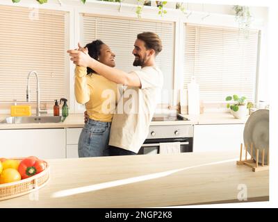 Happy diverse couple having fun dancing together in modern kitchen enjoying lifestyle Stock Photo