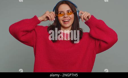 Happy pretty woman in headphones listening music and dancing disco fooling around having fun expressive gesticulating hands, relaxing on party. Caucasian girl isolated on gray studio wall background Stock Photo