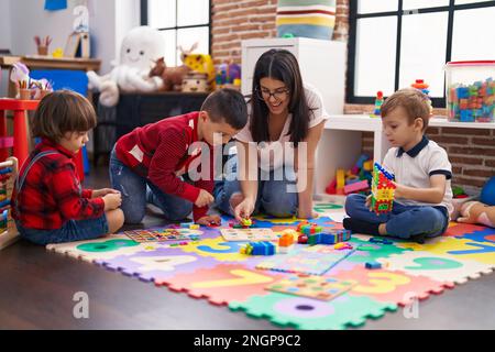 Teacher with group of boys playing with maths puzzle game sitting on floor at kindergarten Stock Photo