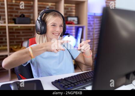 Young caucasian woman playing video games wearing headphones pointing to you and the camera with fingers, smiling positive and cheerful Stock Photo