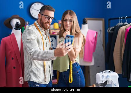 Man and woman tailors smiling confident using smartphone at clothing factory Stock Photo