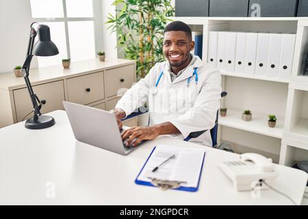 Young african american man wearing doctor uniform sitting on wheelchair working at clinic Stock Photo