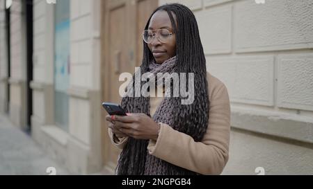 African woman smiling using smartphone at street Stock Photo