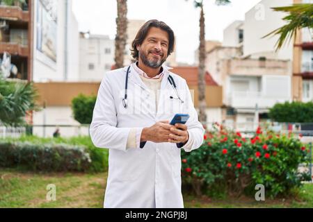 Middle age man doctor smiling confident using smartphone at park Stock Photo