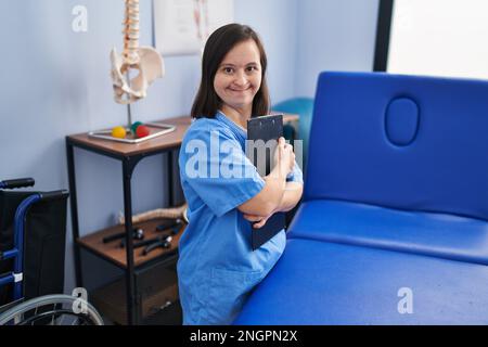 Down syndrome woman wearing physiotherapy uniform holding clipboard at physiotherapist clinic Stock Photo