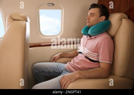 Young man with travel pillow sleeping in airplane during flight Stock Photo