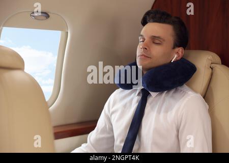 Young man with travel pillow resting while listening to music in airplane during flight Stock Photo
