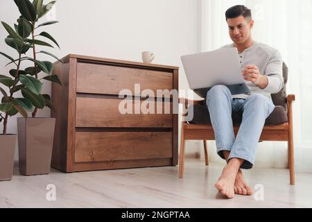 Man with laptop sitting in armchair at home. Floor heating system Stock Photo
