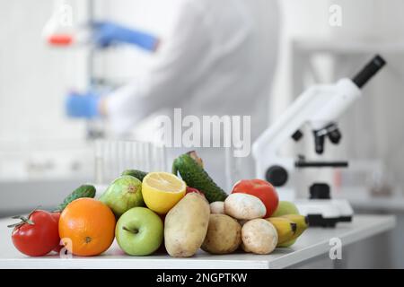 Fresh vegetables, fruits on table and scientist proceeding quality control in laboratory Stock Photo