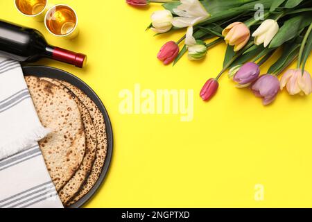 Tasty matzos, wine and fresh flowers on yellow background, space for text. Passover (Pesach) celebration Stock Photo