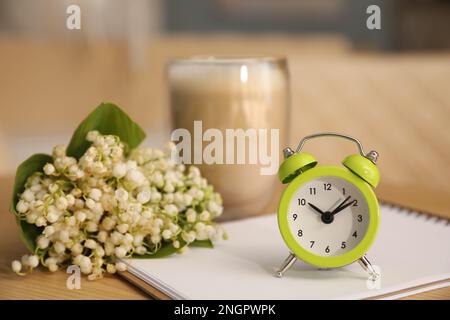 Cup of aromatic morning coffee, notepad, alarm clock and flowers on wooden table in cafe Stock Photo