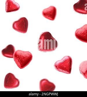 Delicious heart shaped chocolate candies wrapped in red foil falling on white background Stock Photo