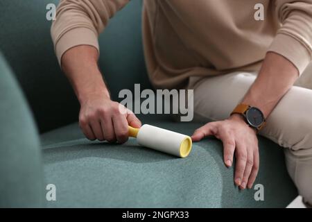Man cleaning sofa with lint roller indoors, closeup Stock Photo