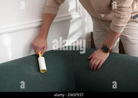 Man cleaning sofa with lint roller indoors, closeup Stock Photo