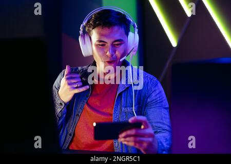 Young male gamer connecting with other video game players and streamers on a video call. Using a smartphone and a headset, a young man engages with a Stock Photo