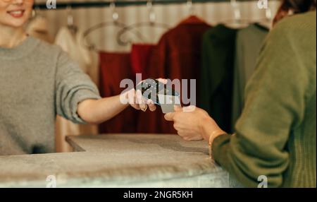 Unrecognisable female customer paying with a credit card at the checkout counter. Young woman tapping a credit card on a contactless card reader. Woma Stock Photo