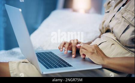 Shes working through the night. an unrecognizable woman using her laptop while relaxing on her bed at night. Stock Photo