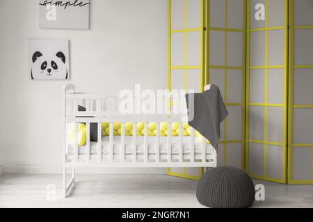 Comfortable crib and folding screen near light wall in children's room Stock Photo