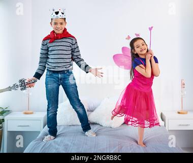 We dont get along all the time. Portrait of two young children dressed up as superheroes jumping on a bed at home. Stock Photo