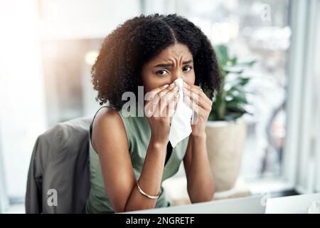 I cant afford to be sick right now. Cropped portrait of an attractive young businesswoman blowing her nose while sitting at her desk in the office. Stock Photo