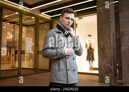 Young man walking down street, autumn or winter cold day. Outdoors, outside. Gorgeous guy in gray coat in city street Stock Photo