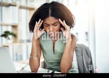 Headaches really bring down productivity. an attractive young businesswoman suffering with a headache while sitting at her desk in the office. Stock Photo
