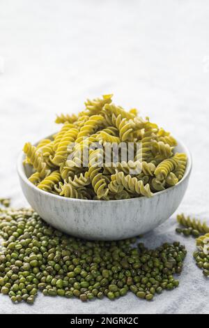 Mung bean fusilli pasta on a gray textile background. Bowl with raw pasta and green mung bean. Gluten free pasta. Stock Photo