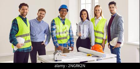 Engineers and architects standing on a building site with architectural plan and smiling Stock Photo
