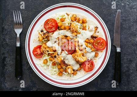 Open-faced vegetable burrito with flour tortillas, cabbage slaw, roasted cauliflower, roasted chickpeas and a spicy sauce. Stock Photo