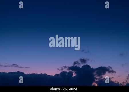 The tranquil beauty of a small crescent moon suspended in a sea of blue and purple hues, peeking out from above the rolling clouds. Stock Photo